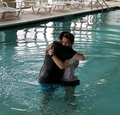 Two people embracing during a baptism in a pool